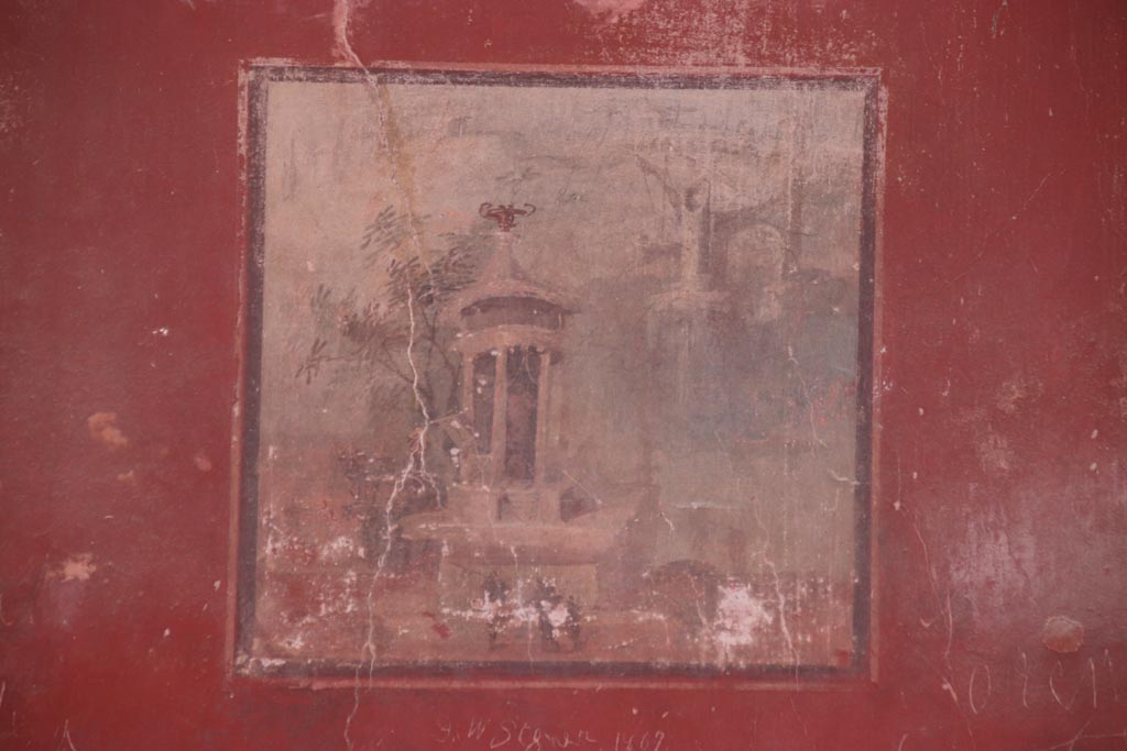 II.2 Herculaneum, October 2023. Detail of landscape painting from north wall. Photo courtesy of Klaus Heese.
According to Maiuri –
“Landscape – Standing amongst trees on the bank of a stream or the sea, an elegant building with Corinthian columns, erected on rocky cliffs: on one side, on a base, a chariot; below are three backlit figures splashed in the usual impressionist manner; in the background, indistinct lines of distant buildings.”
(Paesaggio – Campeggia fra alberi sulla ripa d’un corso d’acqua o del mare, un elegante edificio monoptero a colonne corinzie, eretto su balze rocciose: da un lato, su un basamento, una biga; in basso tre figure controluce schizzate alla consueta maniera impressionistica; nello sfondo, linee indistinte di edifici lontani.)
See Maiuri, A., 1958. Ercolano, I Nuovi Scavi, (1927-1958). Roma: Inst. Poligrafico dello Stato, (p.366).